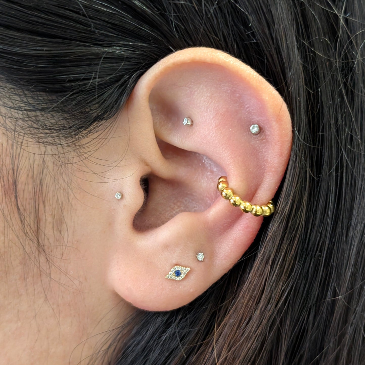 Close‑up of De Mani gold beaded mini ear cuff styled on helix—no piercing needed.