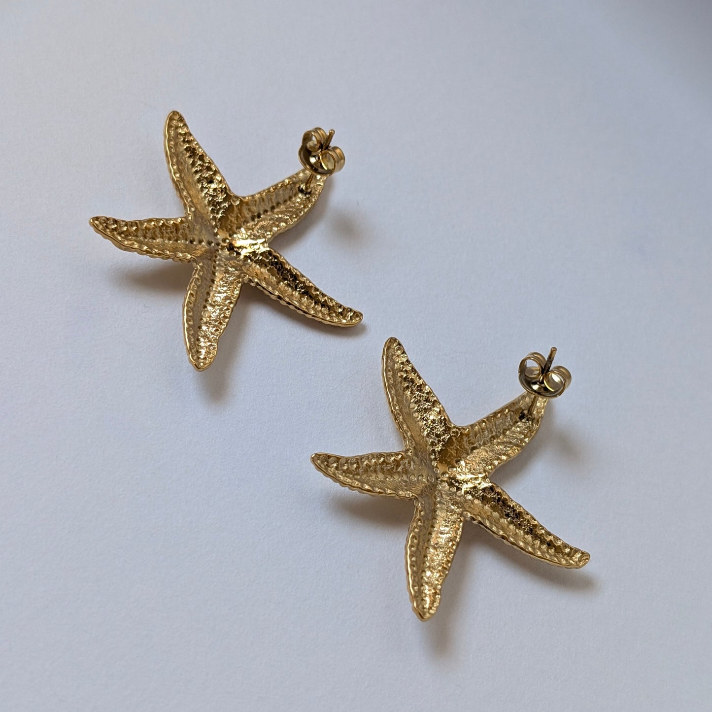 Flat‑lay of waterproof, tarnish‑resistant gold starfish stud earrings on white backdrop.