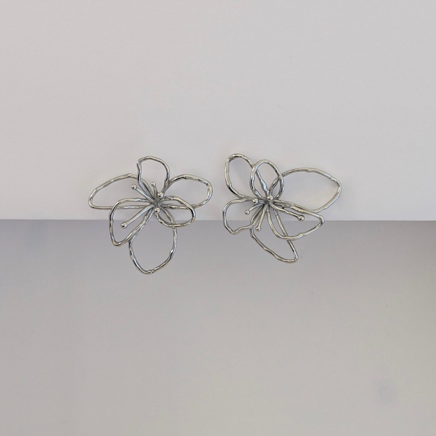 Front view of silver orchid statement earrings—polished stainless steel, sculptural petals, 4 × 4.21 cm studs.