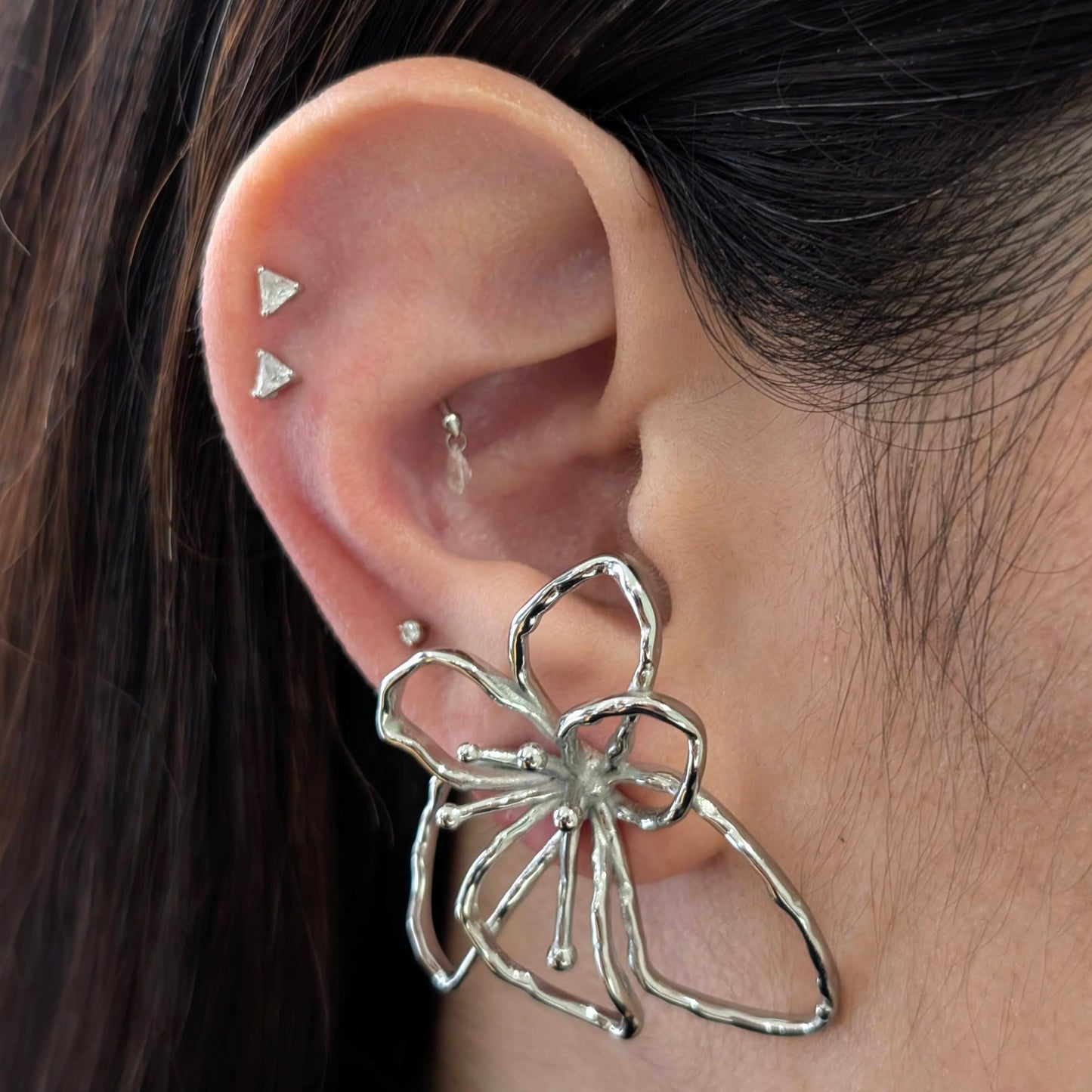 On‑ear close‑up of silver orchid statement earrings—polished stainless‑steel floral studs, 4 cm size.