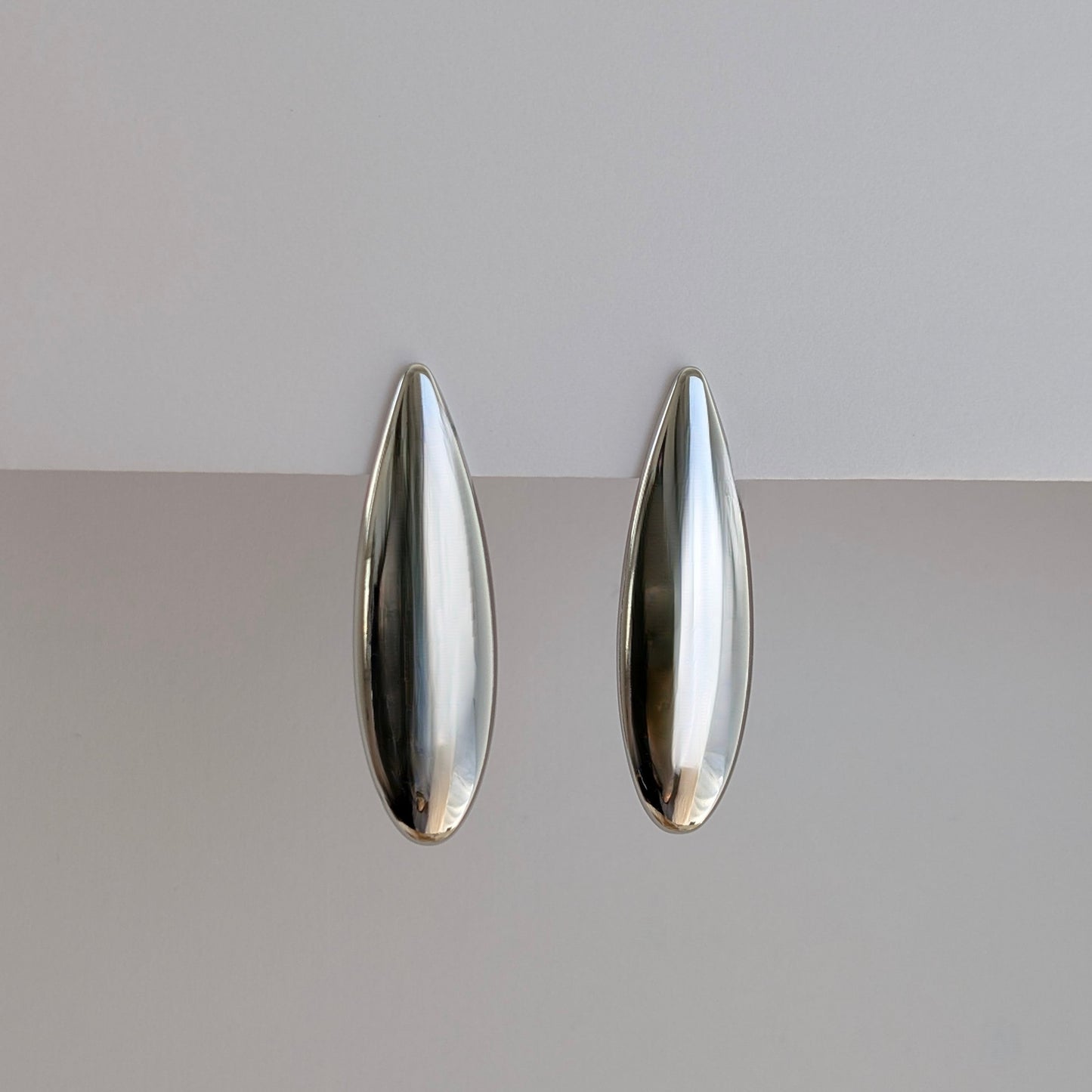 Side angle showing sleek teardrop profile and lightweight 10 g pair of silver statement earrings.